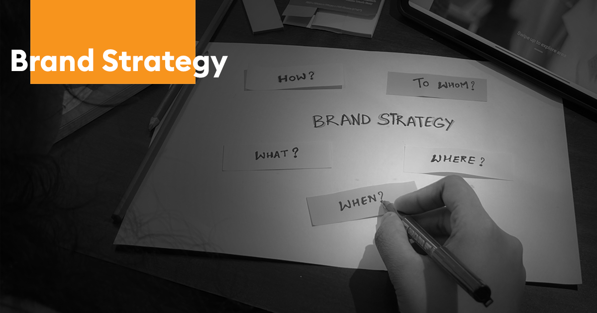 Brand strategy concept image showing a person writing on a planning sheet with questions like “How?”, “What?”, “Where?”, “When?”, and “To Whom?” surrounding the words “Brand Strategy.”