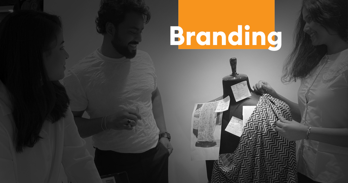 Team members collaborating on fashion branding concepts with fabric samples and a mannequin, alongside the word “Branding” in bold text.